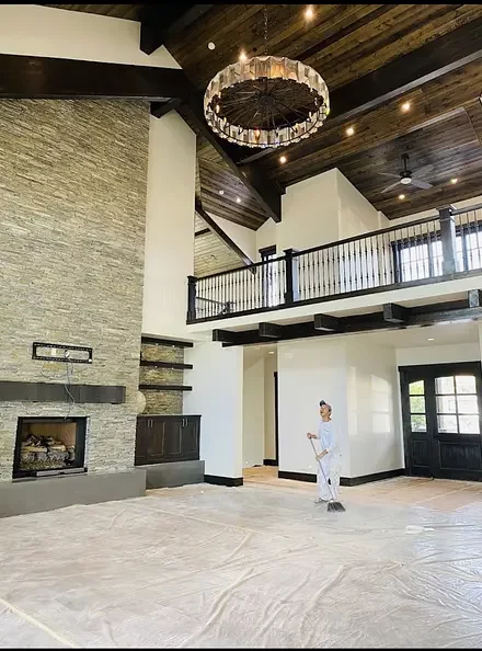 Painter rolling a two-storey great room with a stone fireplace and timber ceiling